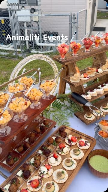 Mesa de banquete de ANIMALITI con canapés, postres y frutas en niveles de madera